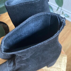 May include: A pair of black suede ankle boots with a zipper on the side. The boots have a low block heel.