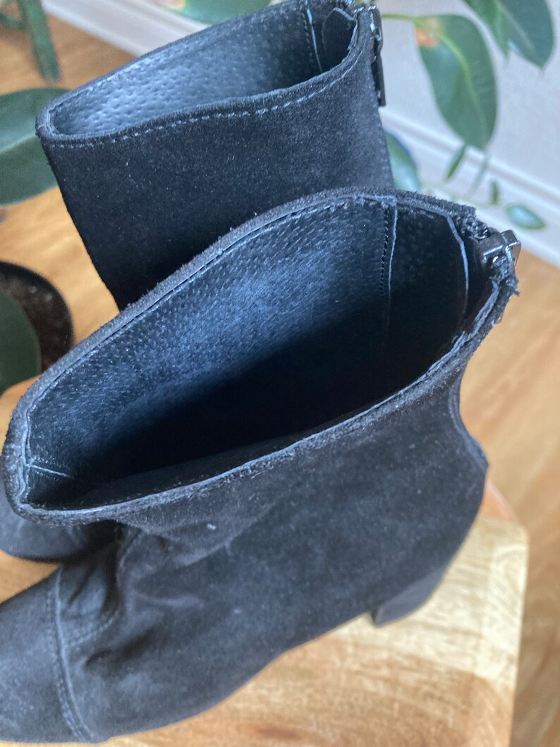 May include: A pair of black suede ankle boots with a zipper on the side. The boots have a low block heel.
