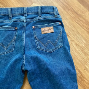 Puede incluir: Un par de pantalones vaqueros azules con un parche de cuero marr&oacute;n en el bolsillo trasero que dice "Wrangler".
