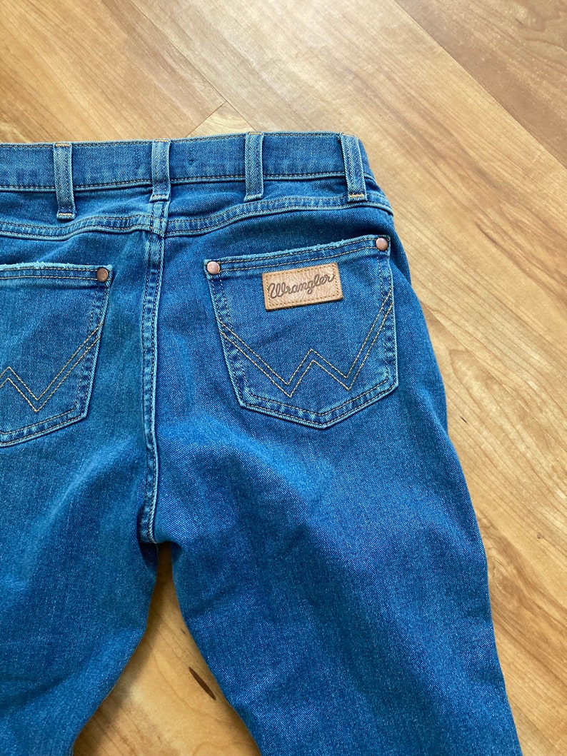 Puede incluir: Un par de pantalones vaqueros azules con un parche de cuero marr&oacute;n en el bolsillo trasero que dice "Wrangler".