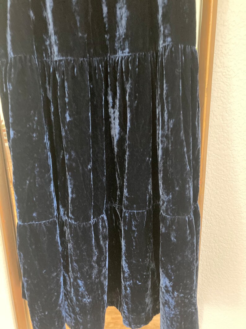 May include: A dark blue velvet dress with a tiered skirt. The dress has a crinkled texture and a loose fit.