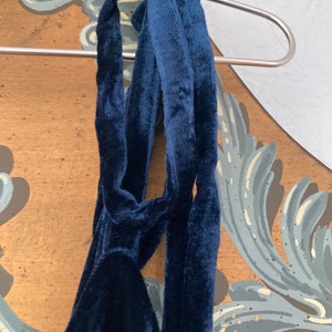 May include: A dark blue velvet halter top with a long, flowing tie. The tie is knotted at the back of the neck.