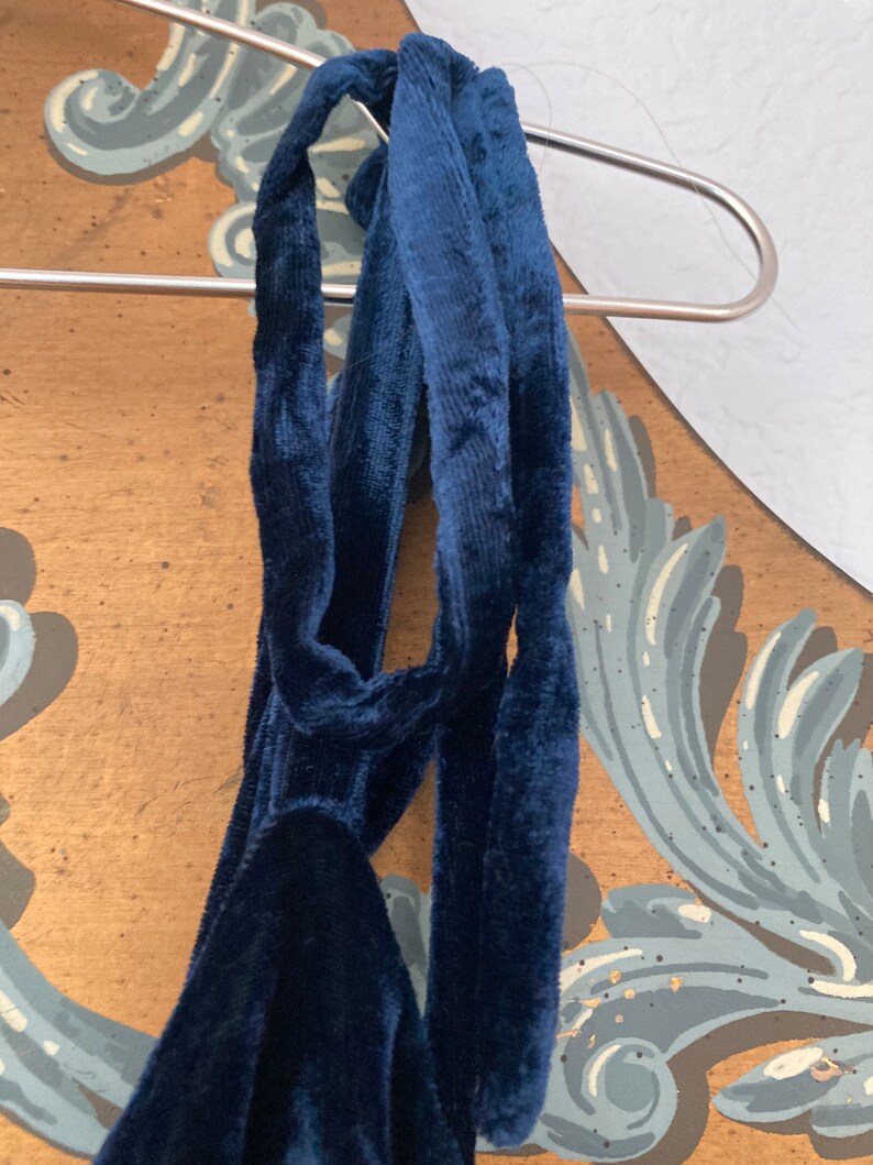 May include: A dark blue velvet halter top with a long, flowing tie. The tie is knotted at the back of the neck.