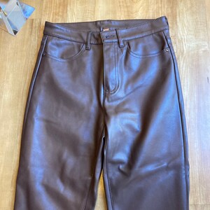 K&ouml;nnte beinhalten: Braune Kunstlederhose mit geradem Bein. Die Hose hat einen Rei&szlig;verschluss und einen Knopfverschluss.