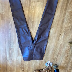 K&ouml;nnte beinhalten: Eine dunkelbraune Kunstlederhose mit schmalem Schnitt. Die Hose hat einen Rei&szlig;verschluss und G&uuml;rtelschlaufen.
