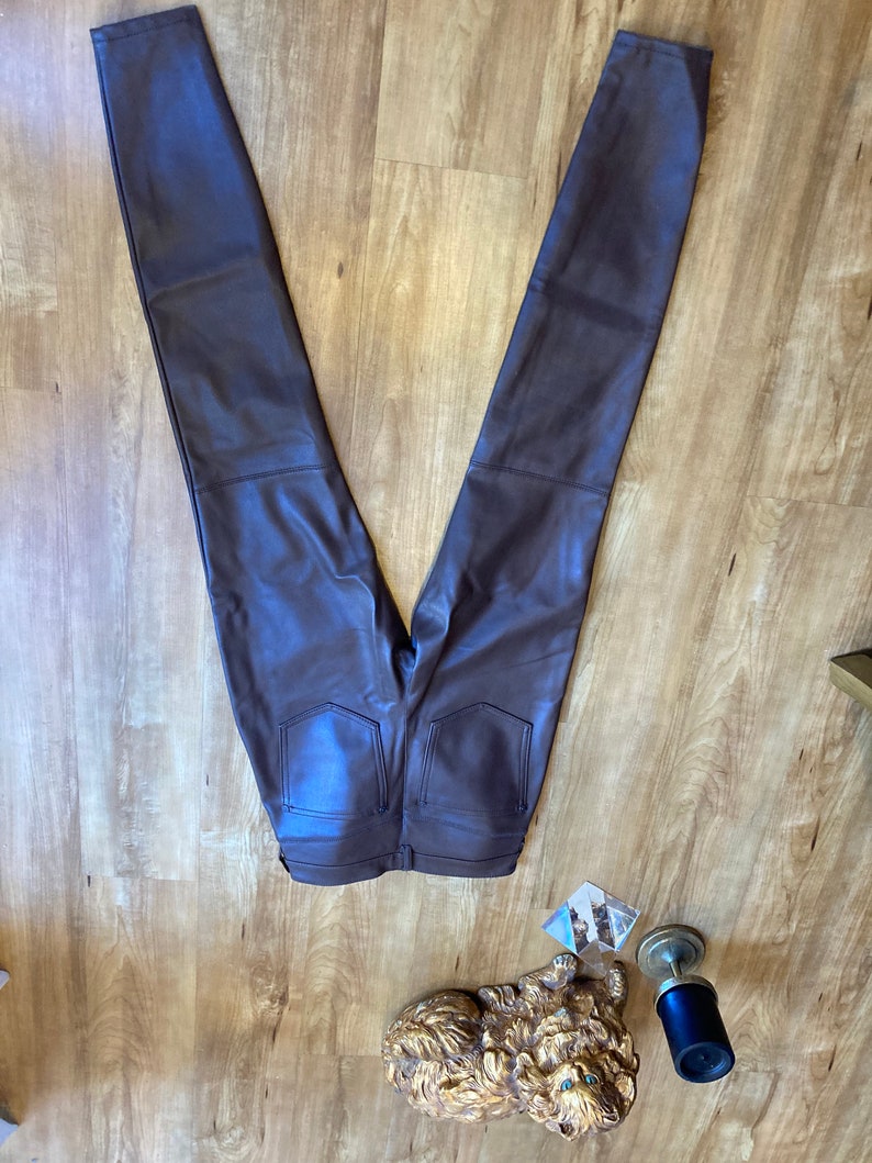 K&ouml;nnte beinhalten: Eine dunkelbraune Kunstlederhose mit schmalem Schnitt. Die Hose hat einen Rei&szlig;verschluss und G&uuml;rtelschlaufen.