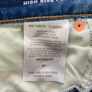 Puede incluir: Una etiqueta blanca con texto negro unida a un par de pantalones vaqueros azules. La etiqueta dice "RN 130273 CA55394 Made in China Hecho en China Fabrique en Chine 80% Cotton/Algodon/Coton 18% Polyester/Poliester/Polyester 2% Spandex/Spandex/Spandex Exclusive of Decoration/Excepto Decoracion/Exclusive of Trimming/Garniture Non Comprise WCHRFPF 25 ZHN-19G-DLBH70593 191057719509"