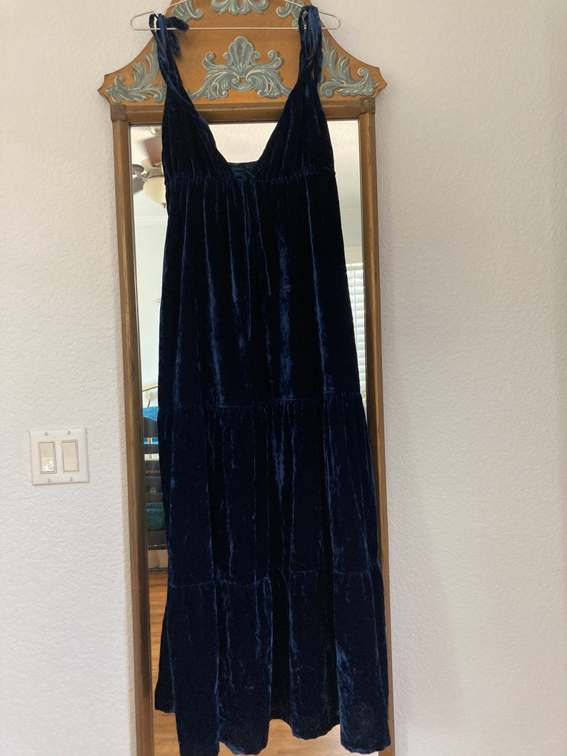 May include: A dark blue velvet maxi dress with a V-neckline and adjustable straps. The dress has a tiered skirt and a gathered waist.