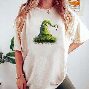 May include: A white t-shirt with a green witch hat with lights on it. The hat is fuzzy and has a pointed tip.