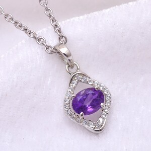 May include: A silver necklace with a pendant featuring a purple amethyst gemstone surrounded by smaller clear gemstones.
