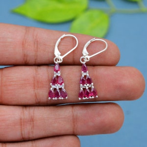 May include: A pair of silver dangle earrings with a triangular design featuring multiple red ruby gemstones.