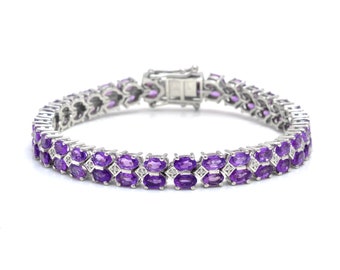 May include: A silver tennis bracelet with a double row of oval-shaped amethyst gemstones and smaller round diamonds.