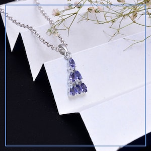 Op de afbeelding: Een zilveren ketting met een hanger met een cluster van paarse amethiststenen in druppelvorm. De hanger is driehoekig en de stenen zijn in drie rijen gerangschikt.