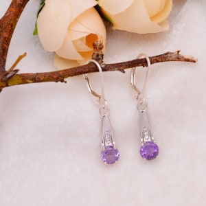 Könnte beinhalten: Ein Paar silberne Ohrhänger mit einem violetten Amethyst-Edelstein und kleinen klaren Zirkonia-Akzenten.
