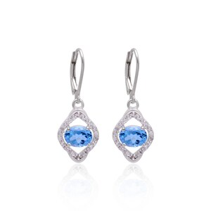 May include: Silver dangle earrings featuring a blue topaz gemstone set within a halo of smaller clear gemstones.