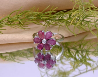 May include: A silver ring with a pink flower design. The flower has a center stone and is surrounded by smaller pink stones.