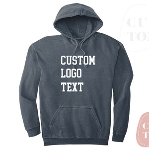 Puede incluir: Una sudadera con capucha azul oscuro con el texto "CUSTOM LOGO TEXT" impreso en blanco en la parte delantera.