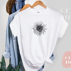 Puede incluir: Camiseta blanca con un dibujo en blanco y negro de un girasol en la parte delantera.