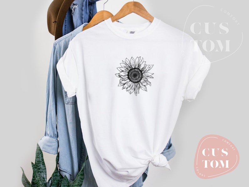 Puede incluir: Camiseta blanca con un dibujo en blanco y negro de un girasol en la parte delantera.