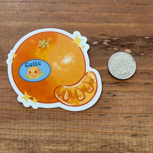 May include: A sticker of a cartoon orange with a smiling face and the word "Cutie" in a blue speech bubble. The orange is orange and yellow with a white background.