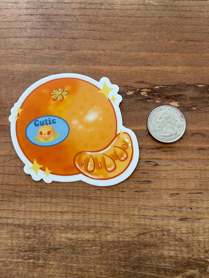 May include: A sticker of a cartoon orange with a smiling face and the word "Cutie" in a blue speech bubble. The orange is orange and yellow with a white background.
