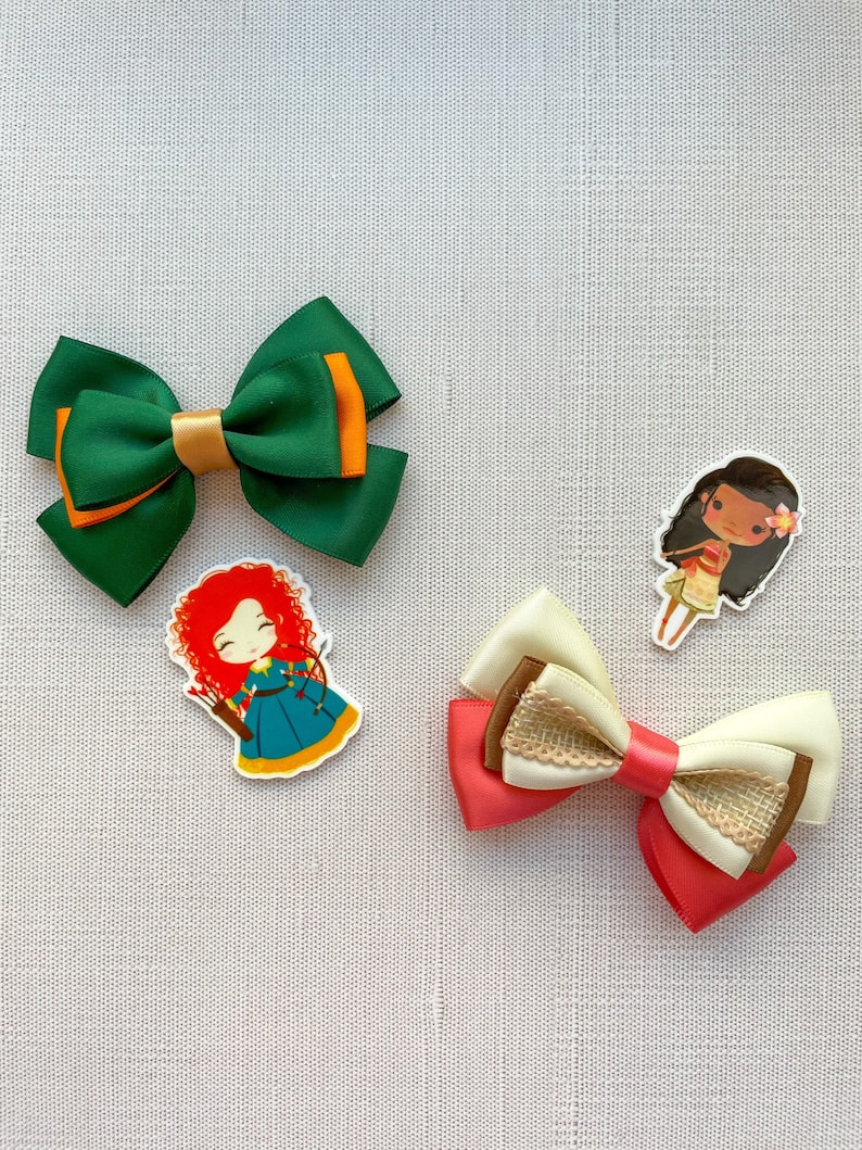 May include: Three hair bows with cartoon character embellishments. The bows are green, pink and white with brown accents. The characters are a girl with red hair, a girl with brown hair and a girl with black hair.