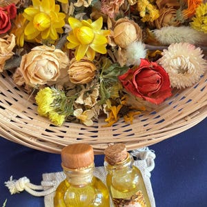 May include: A display of dried flowers in a woven basket, with yellow, orange, and red hues. Two small glass bottles with wooden stoppers and labels are in front of the basket. The bottles contain a yellow liquid.