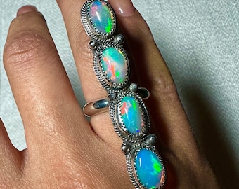 May include: A silver ring with four iridescent opal stones set in a row. The ring is designed to be worn on the middle finger.