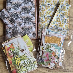 May include: Two rectangular journals with patterned covers, one featuring a black and white floral design and the other a yellow mimosa print. Two clear plastic bags contain assorted paper ephemera, including botanical illustrations and vintage-style cards.