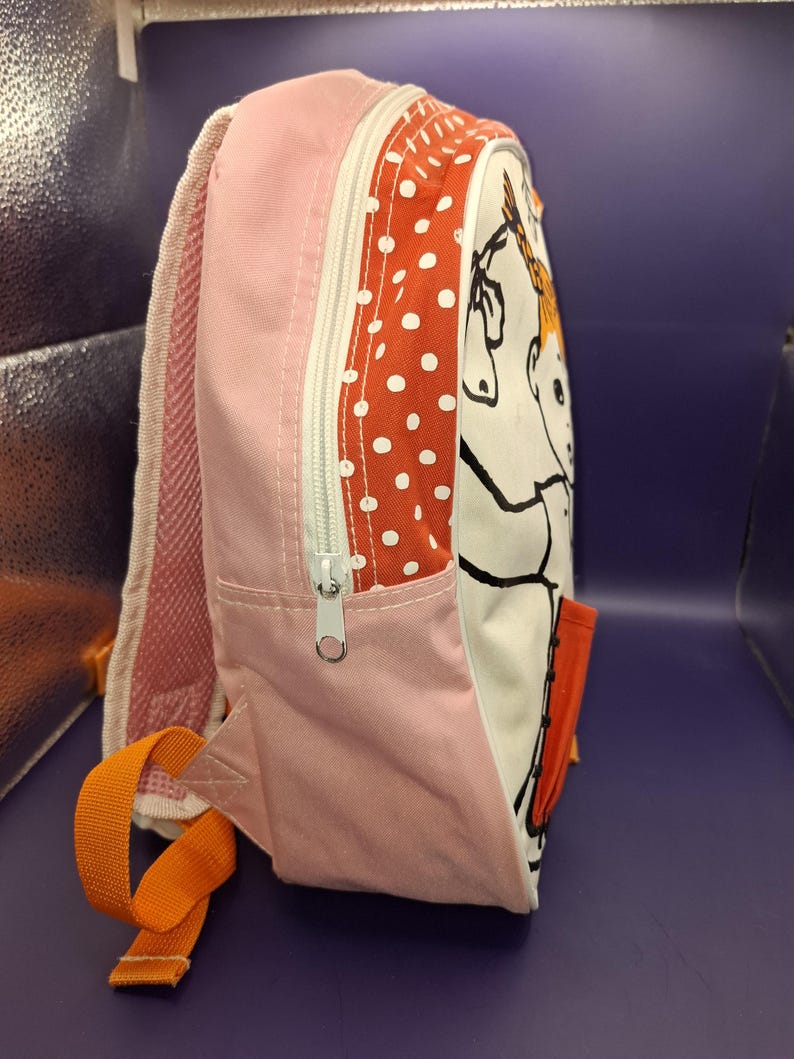 May include: A pink and white children's backpack with a cartoon horse illustration. The bag has a red polka dot pattern, a zip closure, and orange straps. The side features a small pocket. Measurements are in centimetres.