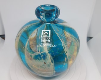 May include: A round, blue glass vase with white and gold swirls. The vase has a small opening at the top and is made by Mdina Crystal Handmade.