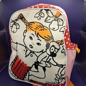 May include: A backpack featuring a cartoon illustration of a girl with orange hair and a monkey. The backpack has a white front with red polka dots, pink sides, and orange straps. The illustration is outlined in black.
