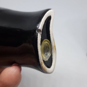 Puede incluir: Primer plano de un tap&oacute;n de botella de cer&aacute;mica negra con un borde blanco y un inserto de vidrio transparente. El tap&oacute;n tiene un peque&ntilde;o agujero en la parte superior.