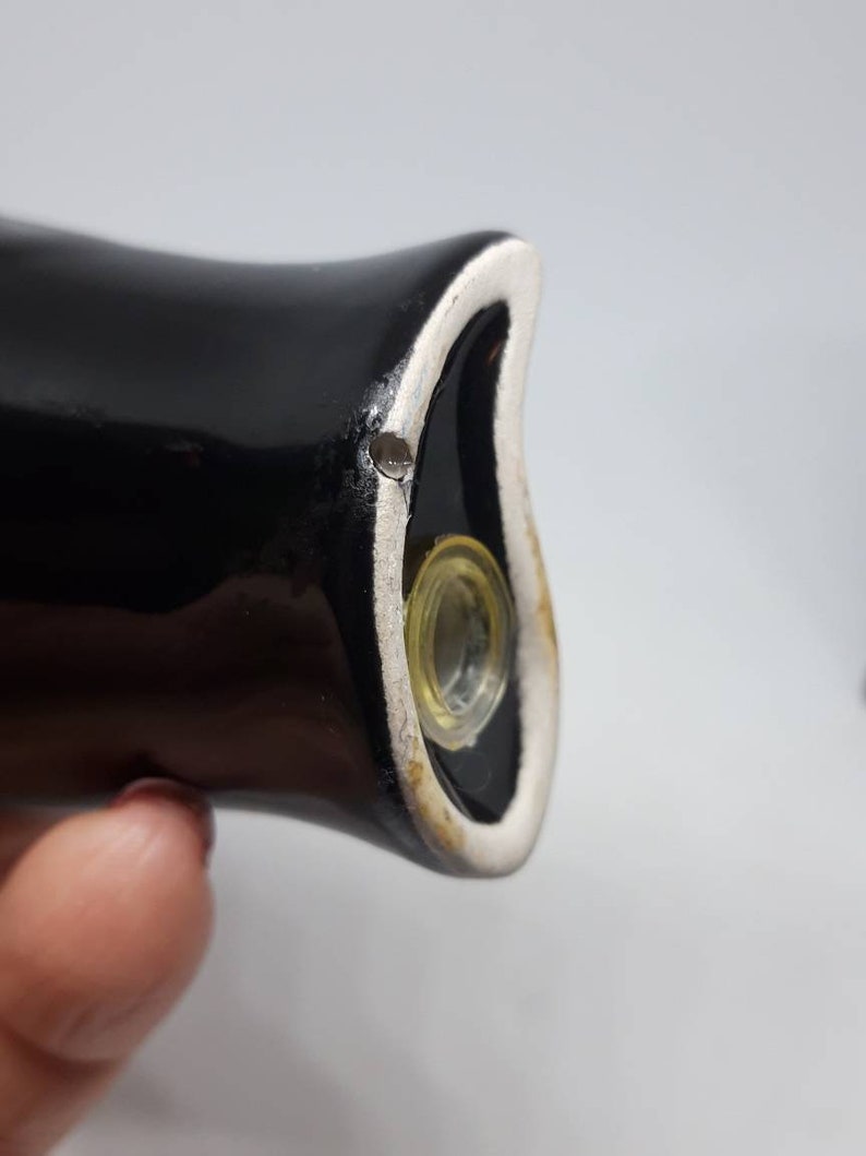 Puede incluir: Primer plano de un tap&oacute;n de botella de cer&aacute;mica negra con un borde blanco y un inserto de vidrio transparente. El tap&oacute;n tiene un peque&ntilde;o agujero en la parte superior.