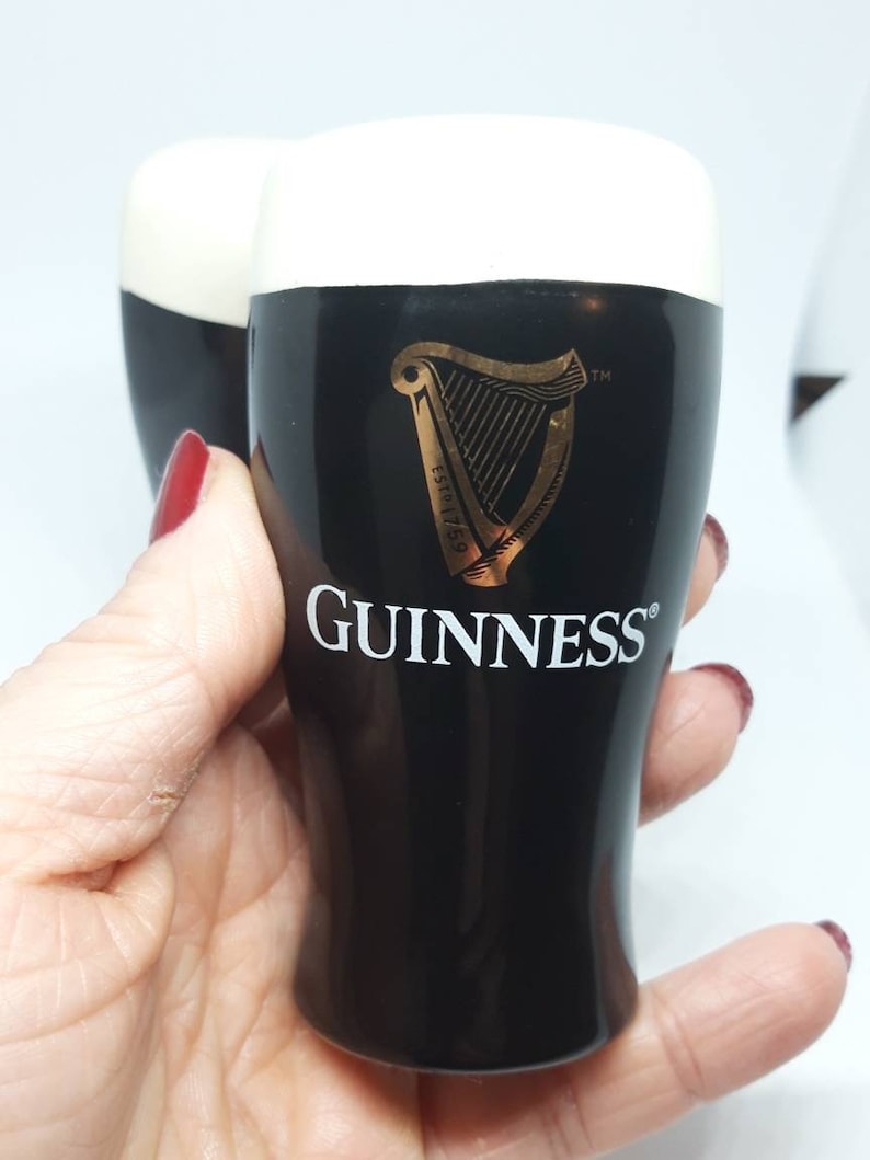 Puede incluir: Dos vasos de chupito de cer&aacute;mica negra con una parte superior de espuma blanca. Los vasos presentan el logotipo de Guinness, un arpa dorada y el texto "ESTD 1778" y "GUINNESS".