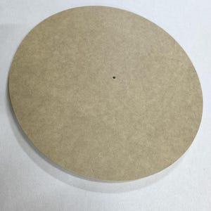 Könnte beinhalten: Eine runde, hellbraune Holzscheibe mit einem kleinen Loch in der Mitte. Die Scheibe hat eine glatte Oberfläche und ist vor einem weißen Hintergrund platziert. Es handelt sich wahrscheinlich um einen Bastelbedarf oder eine Komponente für ein größeres Projekt.