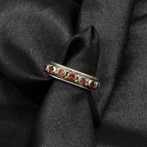 May include: A silver and gold band ring with red gemstones set in a row around the band.