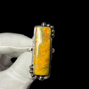 May include: A silver ring featuring a yellow and white agate stone set in a rectangular shape. The ring has a beaded design around the stone.