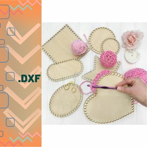 Könnte beinhalten: Eine Sammlung von Häkelbasen aus Holz in verschiedenen Formen, darunter quadratisch, oval und herzförmig, mit vorgebohrten Löchern für Garn. Rosa Garnknäuel und eine Häkelnadel sind ebenfalls vorhanden, zusammen mit einer goldenen Schere. Das Bild zeigt ein laufendes Bastelprojekt.