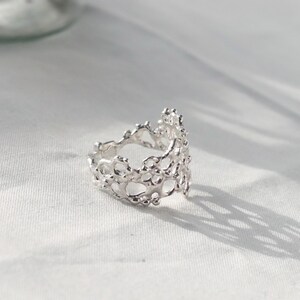 May include: A silver ring with a delicate, intricate design resembling coral. The ring is open and has a textured, organic look.
