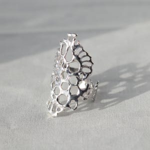 May include: A silver ring with a honeycomb design. The ring is made of a delicate, openwork metal and has a unique, organic shape.