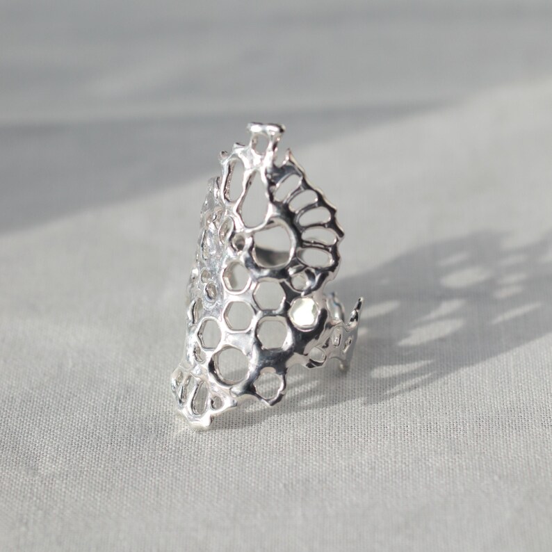 May include: A silver ring with a honeycomb design. The ring is made of a delicate, openwork metal and has a unique, organic shape.
