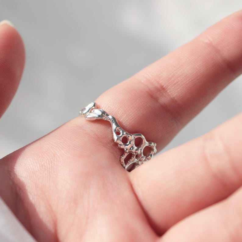 May include: A silver ring with a unique, organic design. The ring is made of a series of interconnected loops and curves, creating a flowing, abstract pattern.
