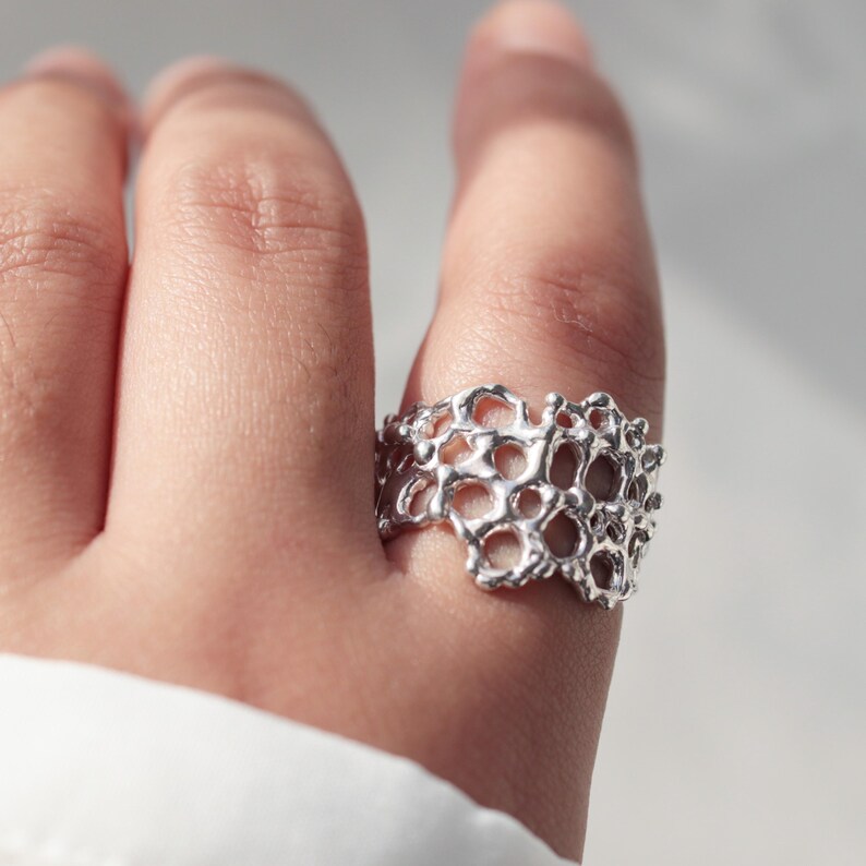May include: A silver ring with a delicate, intricate design resembling coral. The ring is worn on a finger and is a statement piece of jewelry.