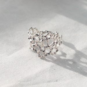 May include: A silver ring with a delicate, intricate design that resembles coral or a honeycomb. The ring is made of a single piece of metal and has a smooth, polished finish.
