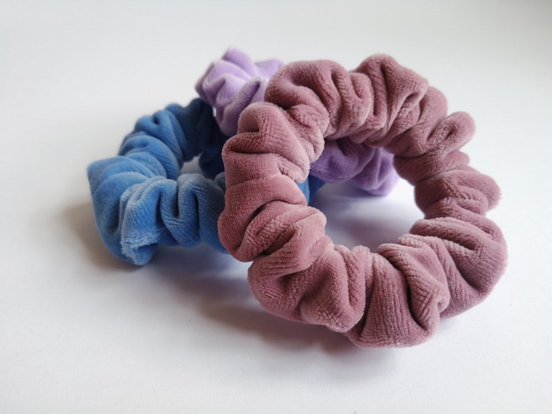 Pu&ograve; includere: Tre scrunchies in velluto in tonalit&agrave; di viola, blu e rosa. Gli scrunchies sono realizzati in un tessuto morbido e peluche e sono perfetti per tenere i capelli in posizione.