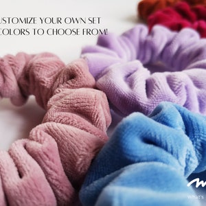 Pu&ograve; includere: Un set di quattro scrunchies in velluto rosa, lavanda, blu e rosso. Gli scrunchies sono disposti in cerchio e il testo "mys. What's your story?" &egrave; visibile in basso a destra.