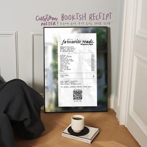 Op de afbeelding: Een ingelijste poster met een aangepast "Bookish Receipt"-ontwerp. De bon vermeldt "favourite reads" met boektitels, data en een QR-code. Een witte koffiekop staat op een boek met een zwarte onderzetter.