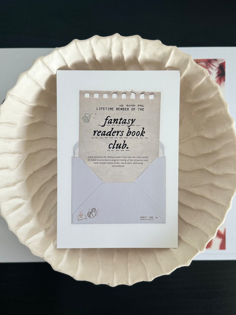 May include: A brown and white card with the text "all access pass LIFETIME MEMBER OF THE fantasy readers book club." The card is in the shape of an envelope with a small illustration of a cat reading a book in the lower left corner.