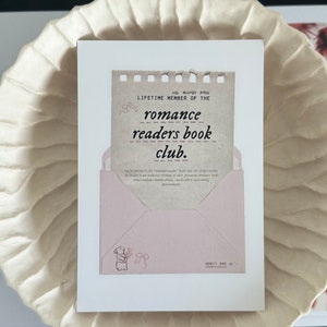 May include: A pink and brown card with the text "all access pass LIFETIME MEMBER OF THE romance readers book club." The card is folded into an envelope with a small illustration of a bunny holding flowers. The envelope has the text "ADMIT ONE" on the bottom.